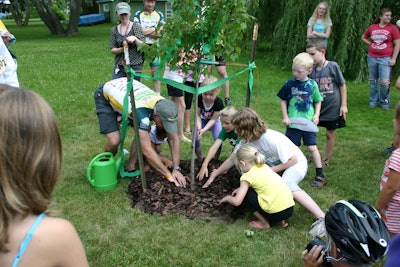 Children of Seymour help spread mulch at the base of the dedicated tree.