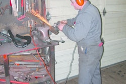 Dealership technician sharpening lawnmower blades with a powered handheld grinder. Some still prefer this method.