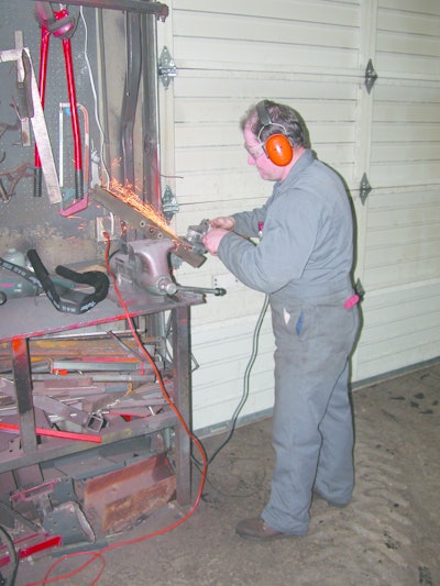 Dealership technician sharpening lawnmower blades with a powered handheld grinder. Some still prefer this method.