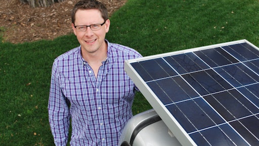 Kelly Giard standing next to a truck outfitted with the Clean Air Solar Charging Unit: mounted solar panels that charge the electric mowers and other equipment throughout the day.