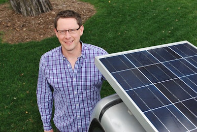 Kelly Giard standing next to a truck outfitted with the Clean Air Solar Charging Unit: mounted solar panels that charge the electric mowers and other equipment throughout the day.