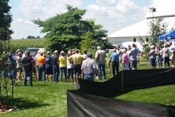 Open house attendees gather around a bare root tree planting demonstration.