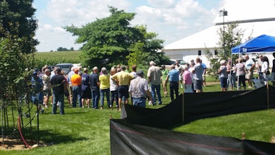 Open house attendees gather around a bare root tree planting demonstration.