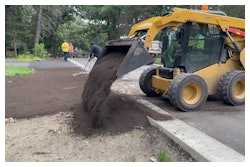 A skid steer laying dirt to prepare the area for sod.