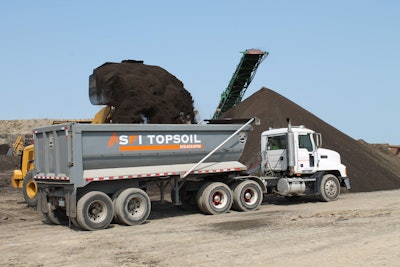 An SFI Topsoil truck is loaded for a dirt delivery with a conveyor in the background.