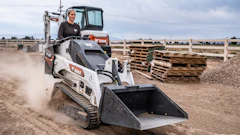 Bobcat MT60 skid-steer loader working on dusty construction site with pallets