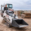 Bobcat MT60 skid-steer loader working on dusty construction site with pallets