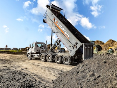 An SFI Topsoil truck unloads dirt at a field.