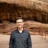 Man in gray shirt and glasses standing near rocky cliff with metal railing Headshot