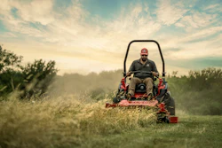 Red zero-turn lawn mower cutting grass at sunset with misty landscape background