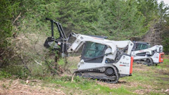 White Bobcat tracked skid steer clearing vegetation in wooded area