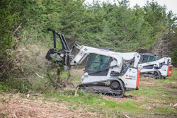 White Bobcat tracked skid steer clearing vegetation in wooded area