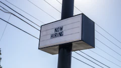 Black and white 'NOW HIRING' sign mounted on utility pole with power lines in background