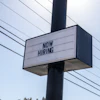 Black and white 'NOW HIRING' sign mounted on utility pole with power lines in background