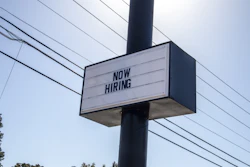 Black and white 'NOW HIRING' sign mounted on utility pole with power lines in background