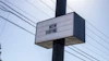 Black and white 'NOW HIRING' sign mounted on utility pole with power lines in background
