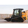 JCB 250T orange tracked skid steer loader on construction site with materials and hillside background