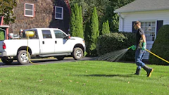 A lawncare technician sprays pesticides on a residential lawn using a hose reel sprayer.