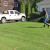 A lawncare technician sprays pesticides on a residential lawn using a hose reel sprayer.