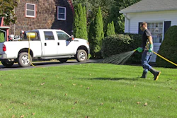 A lawncare technician sprays pesticides on a residential lawn using a hose reel sprayer.