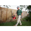 Man in green shirt carrying red yard waste container while walking on grass near wooden fence
