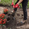 Gardener in red gloves digging holes to plant red flowers in garden soil