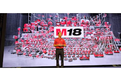 Speaker presenting M18 brand at corporate event with red machinery display backdrop