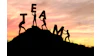 Silhouettes of people forming the word TEAM on a hillside at sunset