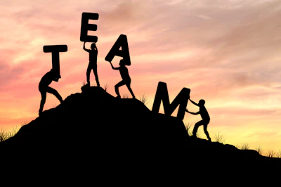 Silhouettes of people forming the word TEAM on a hillside at sunset