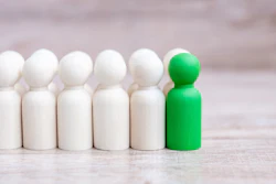 Green peg doll standing out among six white peg dolls on wooden surface