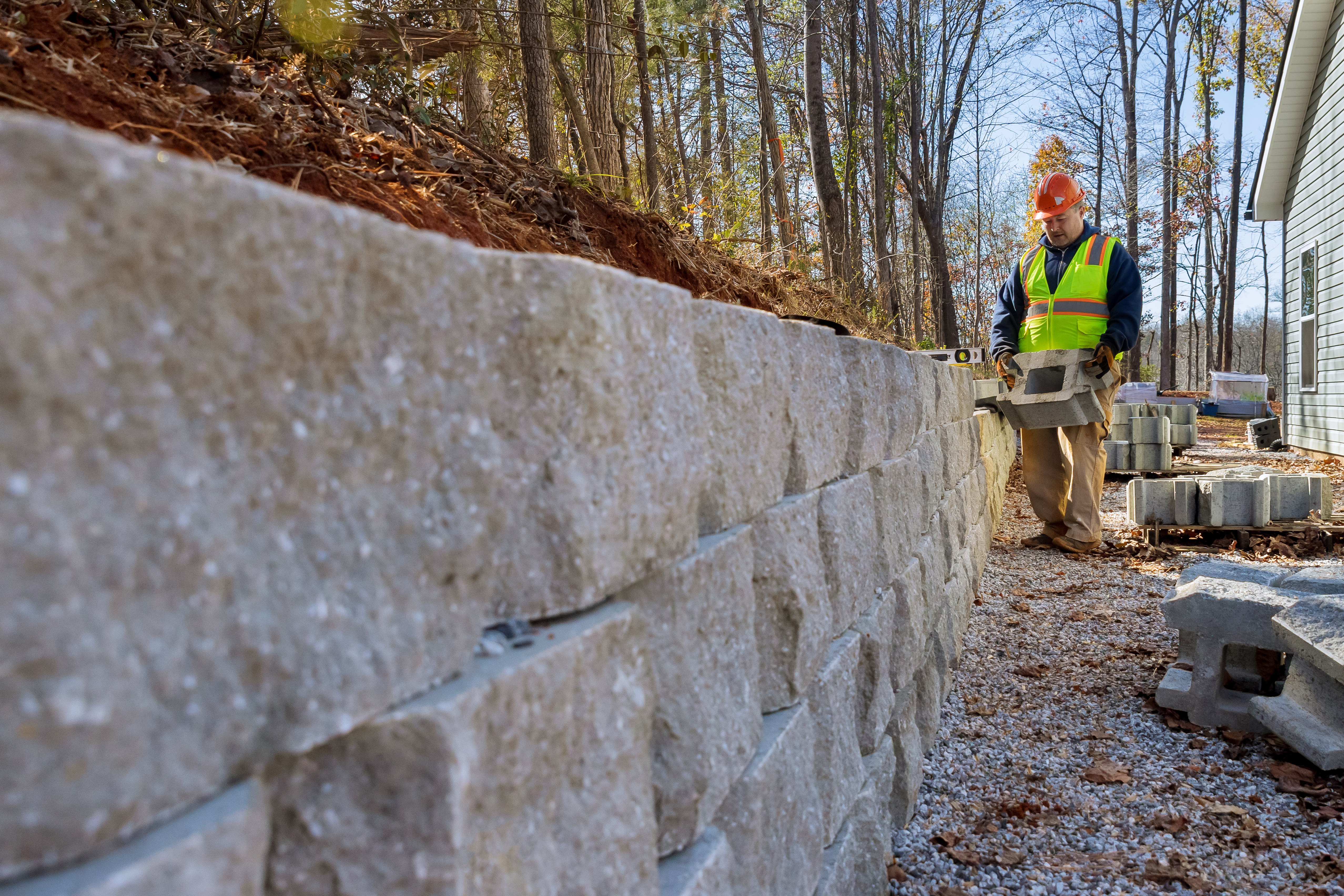 Construction worker in safety vest installing concrete retaining wall on hillside property