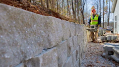 Construction worker in safety vest installing concrete retaining wall on hillside property