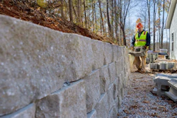 Construction worker in safety vest installing concrete retaining wall on hillside property
