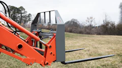 Red telehandler with pallet forks extended in a rural field with bare trees in background