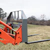 Red telehandler with pallet forks extended in a rural field with bare trees in background