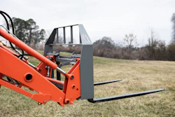 Red telehandler with pallet forks extended in a rural field with bare trees in background