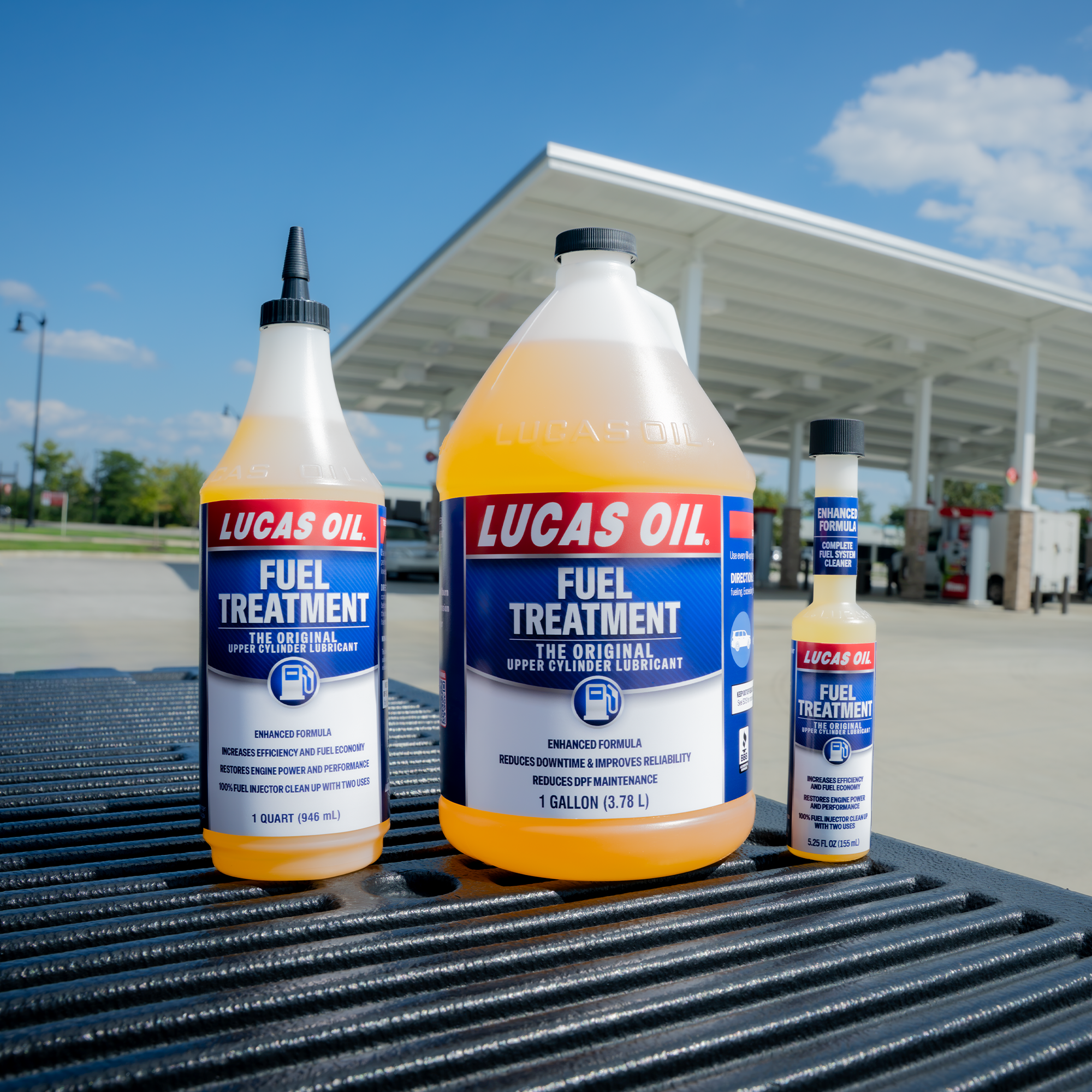 Three bottles of Lucas Oil Fuel Treatment displayed on a truck bed at a gas station with a canopy structure in the background