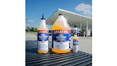 Three bottles of Lucas Oil Fuel Treatment displayed on a truck bed at a gas station with a canopy structure in the background