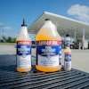 Three bottles of Lucas Oil Fuel Treatment displayed on a truck bed at a gas station with a canopy structure in the background