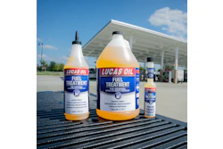 Three bottles of Lucas Oil Fuel Treatment displayed on a truck bed at a gas station with a canopy structure in the background