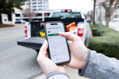 Person holding smartphone displaying engine oil and filter replacement service app with truck in background