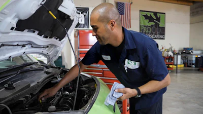 Mechanic inspecting car engine under open hood in service garage with tools and equipment