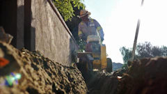 Construction worker operating yellow machinery near concrete wall in outdoor setting