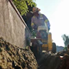Construction worker operating yellow machinery near concrete wall in outdoor setting