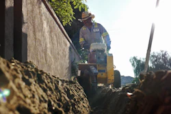 Construction worker operating yellow machinery near concrete wall in outdoor setting