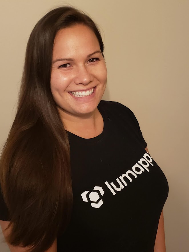 Smiling woman with long dark hair wearing a black Lumaapp branded t-shirt against a neutral beige background