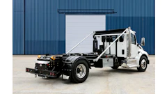 White and black commercial tow truck with hydraulic lift system parked in front of industrial blue corrugated metal building