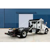 White and black commercial tow truck with hydraulic lift system parked in front of industrial blue corrugated metal building