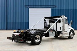 White and black commercial tow truck with hydraulic lift system parked in front of industrial blue corrugated metal building