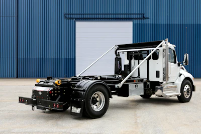 White and black commercial tow truck with hydraulic lift system parked in front of industrial blue corrugated metal building